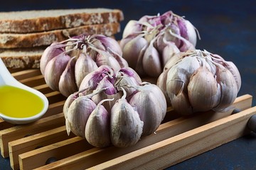 PRIMER PLANO DE AJOS BLANCOS Y MORADOS JUNTO A CUCHARA CON ACEITE DE OLIVA Y PAN RÚSTICO