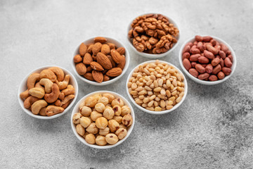 Assortment of nuts in white saucers on a concrete background. Food mix background, top view, copy...