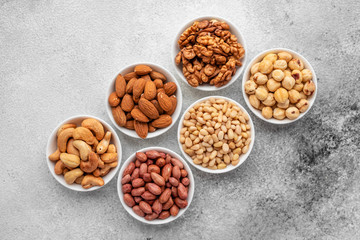 Assortment of nuts in white saucers on a concrete background. Food mix background, top view, copy...
