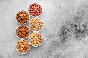 Assortment of nuts in white saucers on a concrete background. Food mix background, top view, copy...