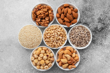 Assortment of nuts in white saucers on a concrete background. Food mix background, top view, copy space, banner