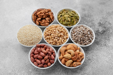 Assortment of nuts in white saucers on a concrete background. Food mix background, top view, copy space, banner