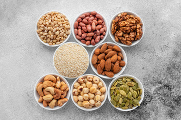 Assortment of nuts in white saucers on a concrete background. Food mix background, top view, copy space, banner