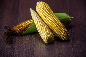 Corn cobs on dark wooden background.