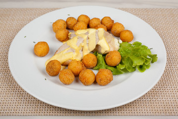 Fried potato balls and chicken fillet with green salad on a white plate.