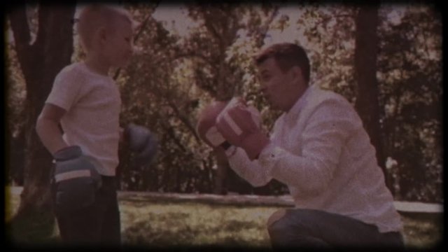 Family video archive. Retro camera 8&nbsp;mm. Old film. Father and son in boxing gloves play boxing on the lawn near the house. happy childhood.