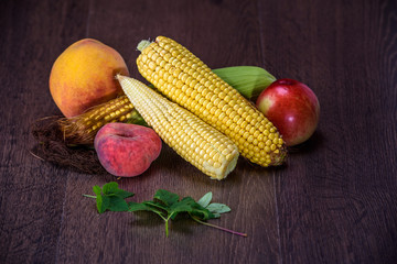 Peaches and corn cobs on a dark wooden background.