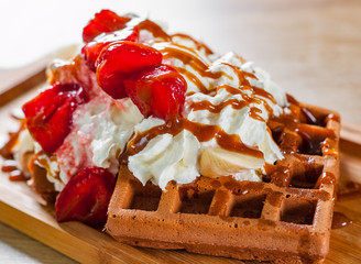 portion of Viennese waffle with cream, strawberry, banana, caramel and ice cream on wooden table...