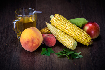 Peaches and corn cobs on a dark wooden background.