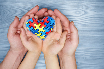 World Autism Awareness day, puzzle or jigsaw pattern on heart with autistic child's and father hands