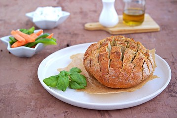 Round baked party bread on a ceramic plate. Served with cream cheese dip and fresh chopped carrots and sweet green pepper. Selective focus
