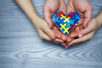 World Autism Awareness day, puzzle or jigsaw pattern on heart with autistic child's and father hands
