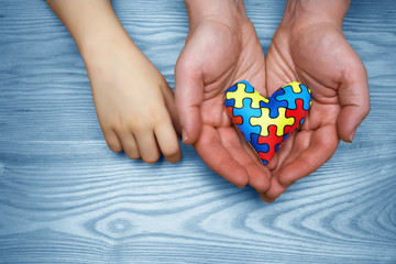 World Autism Awareness day, puzzle or jigsaw pattern on heart with autistic child's and father hands