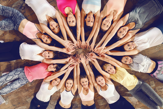Top view of beautiful fit women lying down in circle on the gym floor and holding hands above heads.