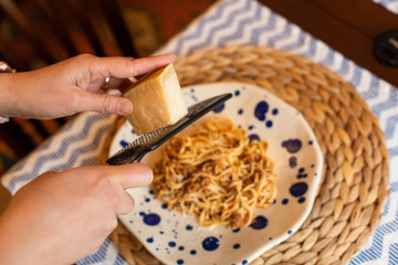 woman hands grating parmesan cheese to homemade spaghetti bolognese, traditional pasta dish with meat and vegetables