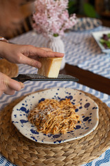 woman hands grating parmesan cheese to homemade spaghetti bolognese, traditional pasta dish with meat and vegetables