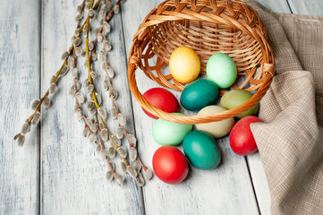 Easter eggs in a basket and willow branches on a wooden background
