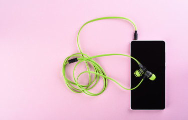 Green earphones connected to a smartphone isolated on a pink background. Accessories for individual listening to audio files.