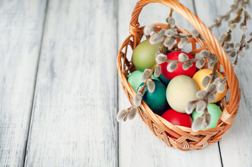 Easter eggs in a basket and willow branches on a wooden background