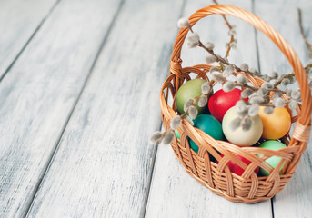 Easter eggs in a basket and willow branches on a wooden background