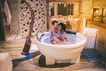 Happy interracial couple relaxed in the jacuzzi enjoying their self and drinking wine .