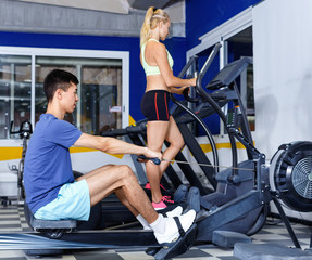 Fototapeta na wymiar Young fitness man and woman doing cardio workout on fitness machines at gym