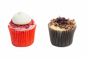 Cupcake in red paper case with pink frosting and raspberry on top and chocolate black forest fairy cake on white, selective focus