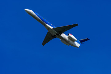 Airplane climbs after takeoff, from the ground with clear blue sky.