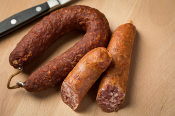 Luftgetrockneter Mettwurst Ring und frische Bierbeißer, zwei Salami Sorten aus Schweinefleisch mit Messer auf Holz Brett 