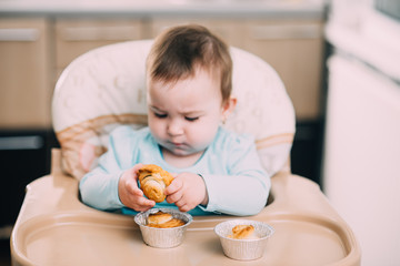 the little girl in the highchair in the hands Krapina, like muffins and croissants trend 2019