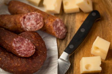 Ringwurst Salami, Bierbeißer Wurst und Edamer Käse in Wachspapier mit Messer auf Vesper Holzbrett