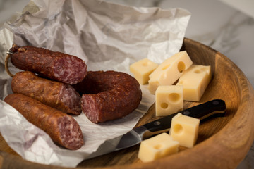 Ringwurst Salami, Bierbeißer Wurst und Edamer Käse in Wachspapier mit Messer auf Vesper Holzbrett