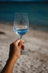 blue sea background wine glass with brilliant liquid natural light tanned female hand