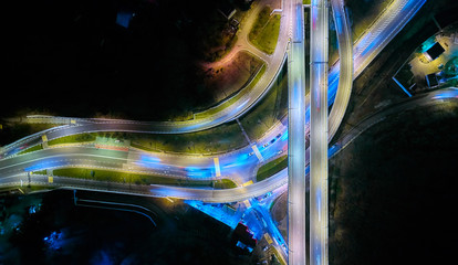Aerial drone night shot of multilevel illuminated ring highway road junction leading to the sea,...