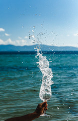 Aquamarine sea background with blue sky and white clouds skyline spray water drops from wine glass with brilliant liquid natural light tanned female hand and shadows and caustic landscape