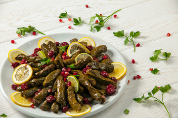 Stuffed wine leaves. Cherry and lemon leaf wrapping, stuffed. Traditional Turkish stuffed leaf wrapper. Decorated with cherry, lemon, parsley and pomegranate seeds. Wooden pattern on white background.