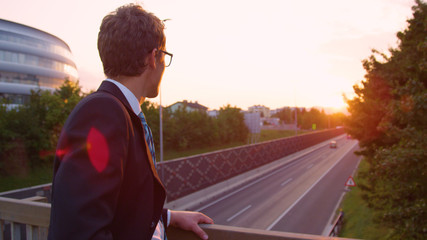 CLOSE UP: Young businessman lost in thought watches the busy highway below him.