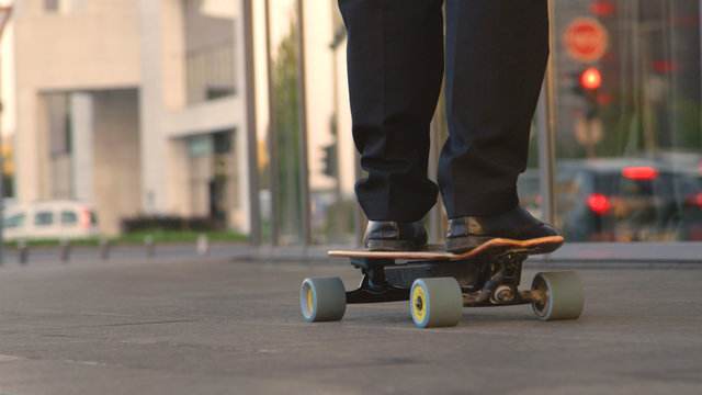 LOW ANGLE: Unrecognizable businessman longboarding through city on sunny evening