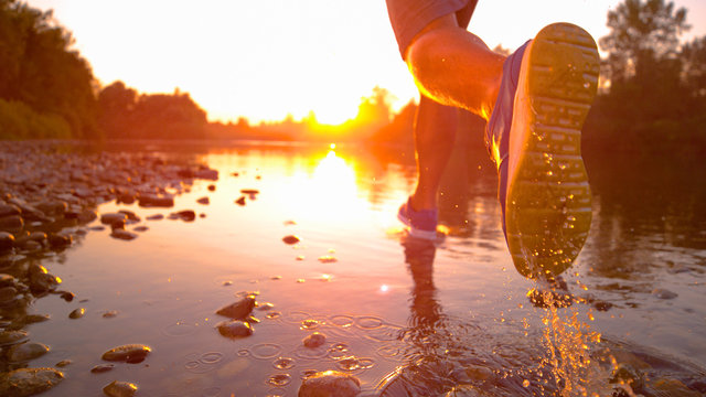 LENS FLARE, CLOSE UP Unrecognizable sportsman jogging in shallow river at sunset