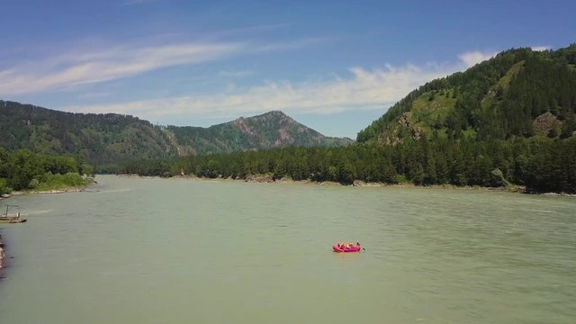Aerial: Flying over mountain river. Also visible: coniferous forest, rapids on the river, bank of the river red boat, with people engaged in rafting on the river, who row with oars.