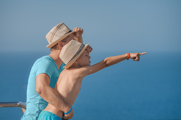 Son and dad relaxing on hotel balcony on summer holidays. Father is holding son on hands.