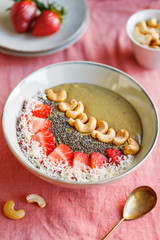 Green smoothie bowl with coconut cream, banana, strawberry, cashew and chia seeds. Healthy vegan eating.