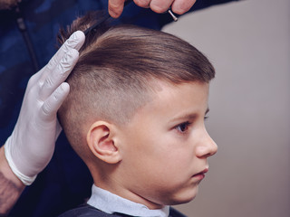 Side view of cute boy getting hairstyle by hairdresser in barbershop. - 254995306