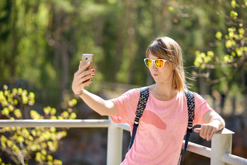 Young European girl is taking selfie photo against picturesque landscape.