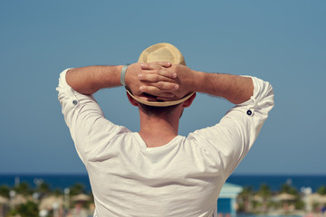 Attractive European man in sunhat is observing wonderful hotel’s view.