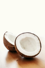 Halved coconut on wooden table in white light. Hello summer vacation concept. Space for text. Tropical background with coconut. Delicious nut, refreshing drink and oil source, tasty milk