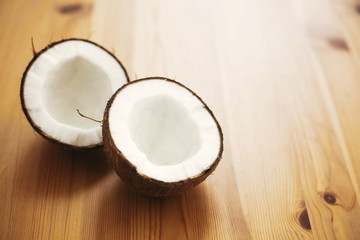 Halved coconut on wooden table in white light. Hello summer vacation concept. Space for text. Tropical background with coconut. Delicious nut, refreshing drink and oil source, tasty milk