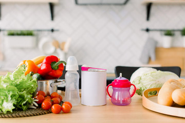 healthy foods are on the table in the kitchen. Fresh vegetables and fruits, baby food, bread and milk on the wooden table, modern kitchen blurred background