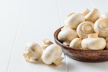 Brown clay bowl with mushrooms on white wooden table. Vegetarian cuisine.