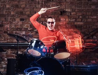 Fototapeta na wymiar Young Stylish musician in sunglasses emotionally playing drums against brick wall background, perform in a night club. Photo with lighting motion effect